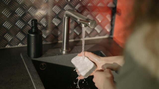 person holding white paper near stainless steel faucet