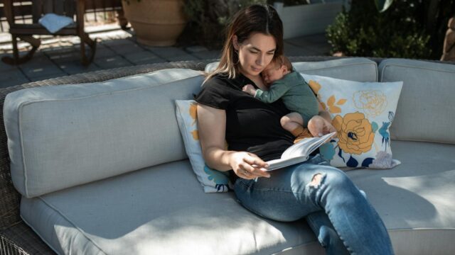 woman in black shirt and blue denim jeans sitting on gray couch reading book