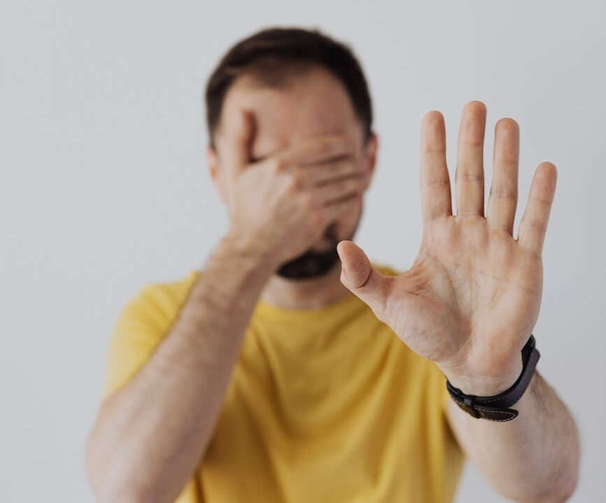 man covering his face with his hand and showing a stop sign gesture